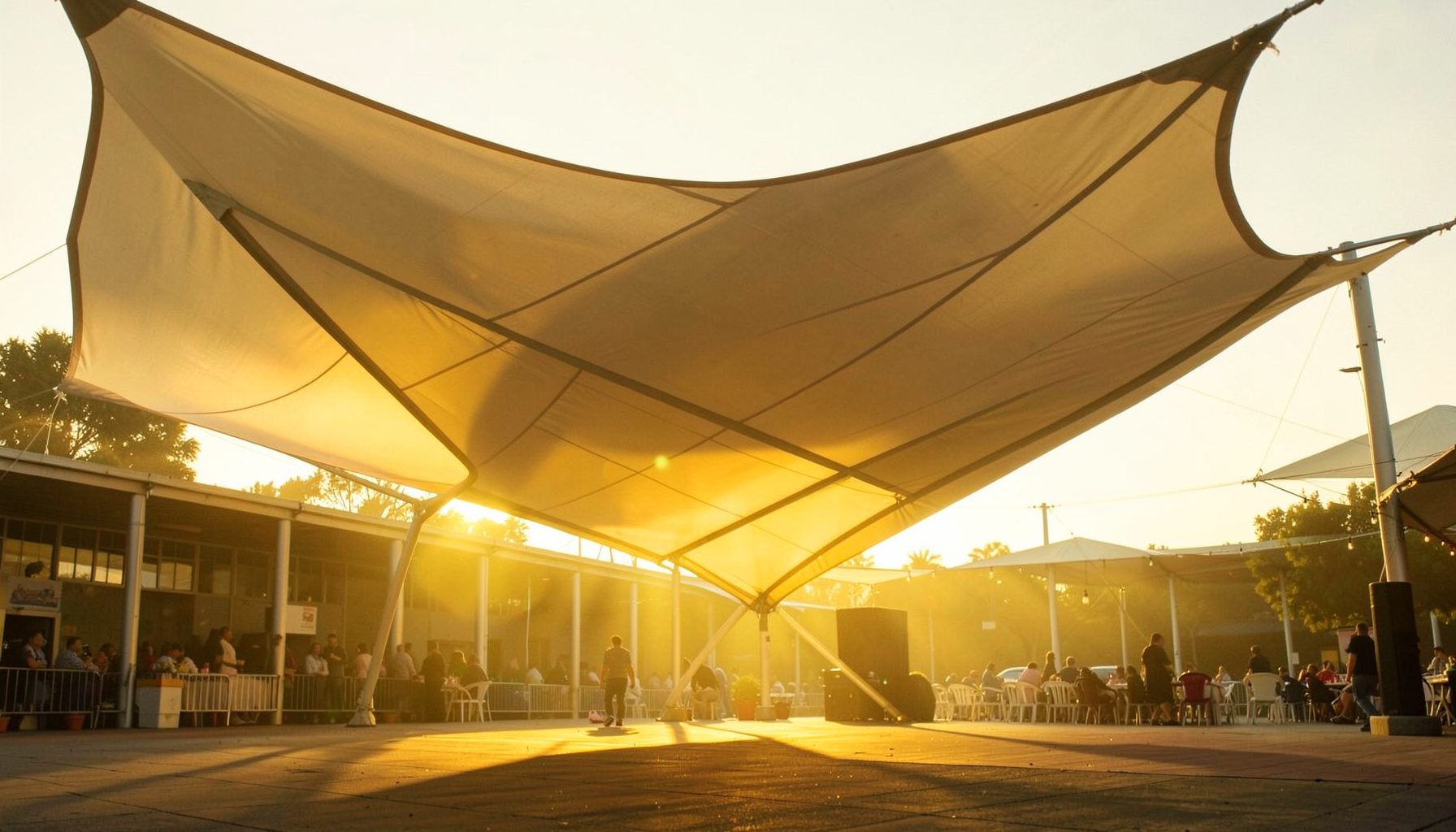Architectural membrane structure canopy at a public venue, PTFE-coated fabric stretched taut under warm evening sunlight