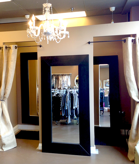Boutique fitting room area with large dark-framed mirrors, chandelier, and beige curtains, elegant clean mood